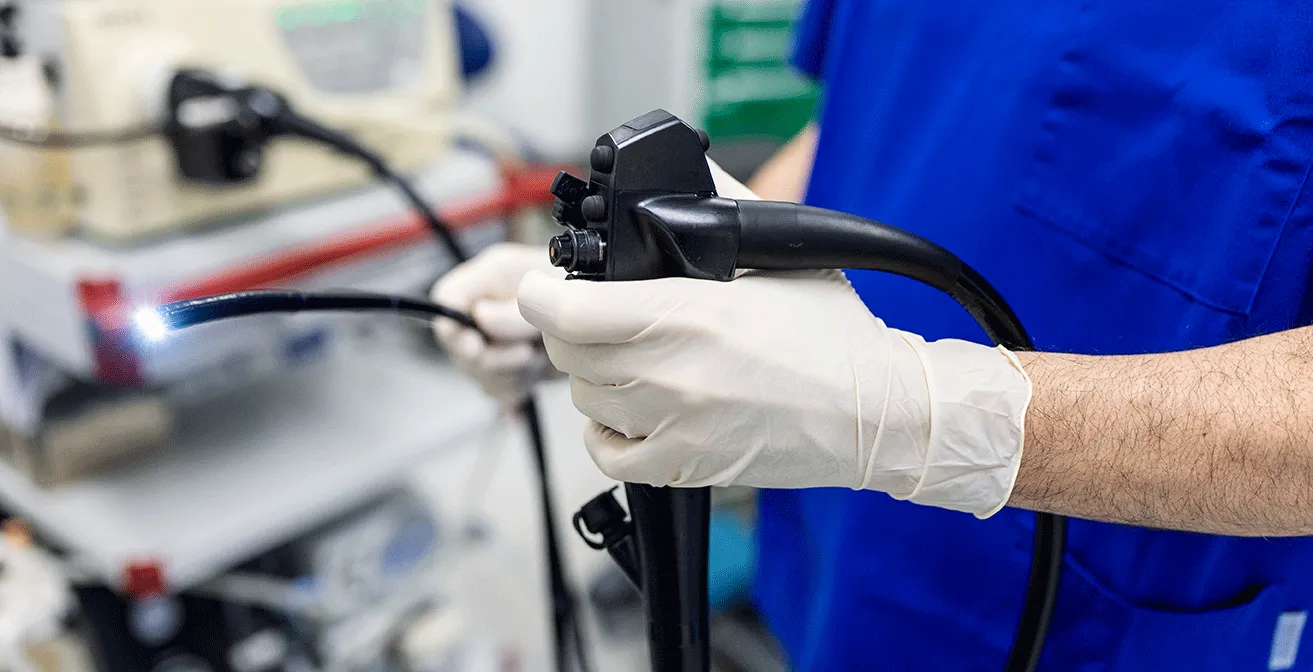 Surgeon wearing blue surgical gloves holding an endoscope during a gastroscopy or endoscopic procedure.