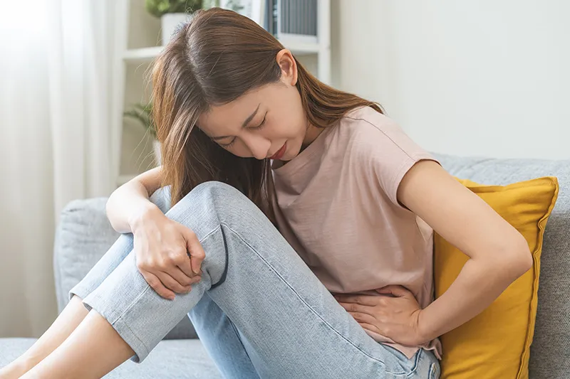 Woman experiencing abdominal pain, holding her stomach while seated.